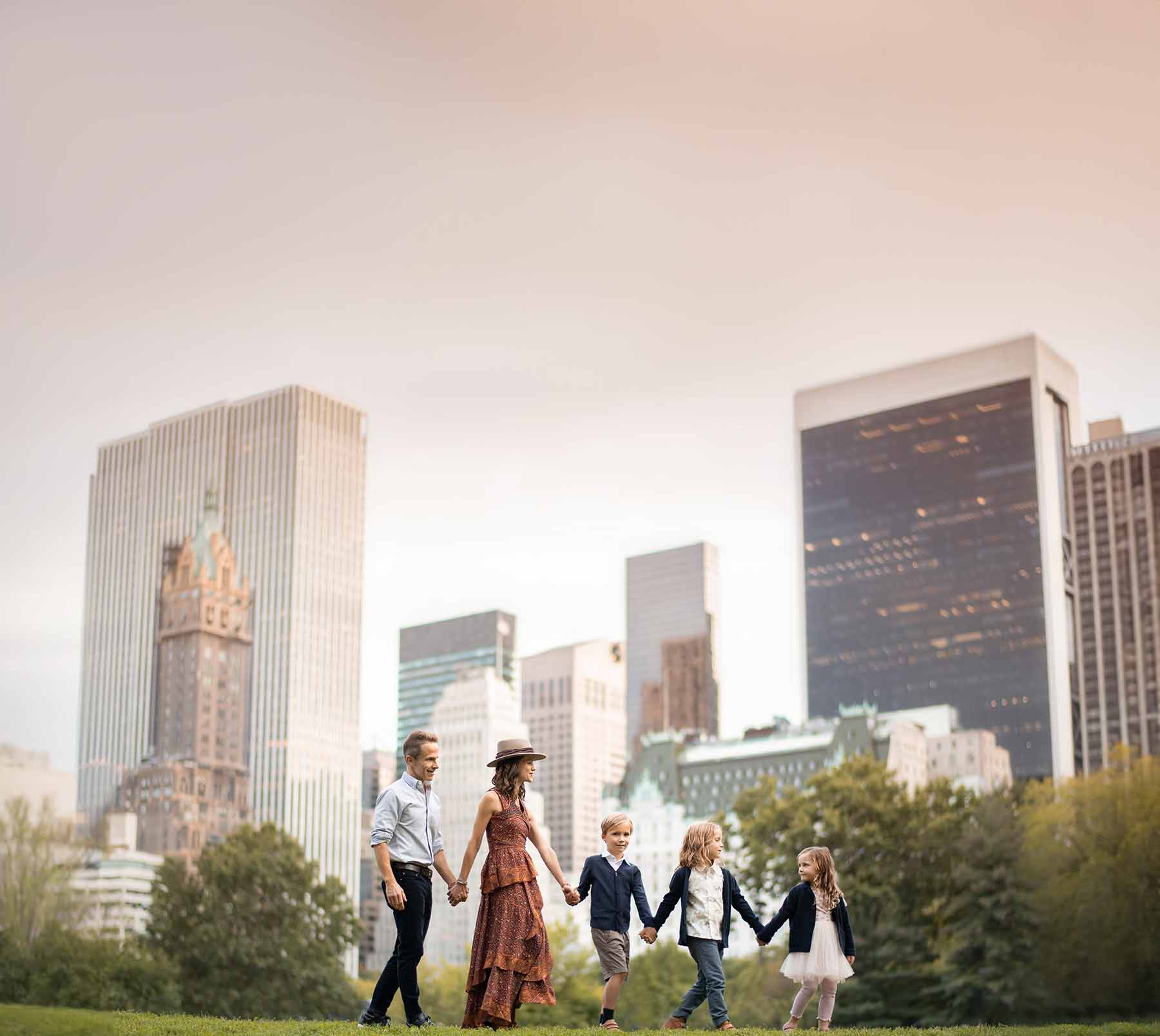 A stylish NYC family walking in Central Park with the midtown skyline behind them.