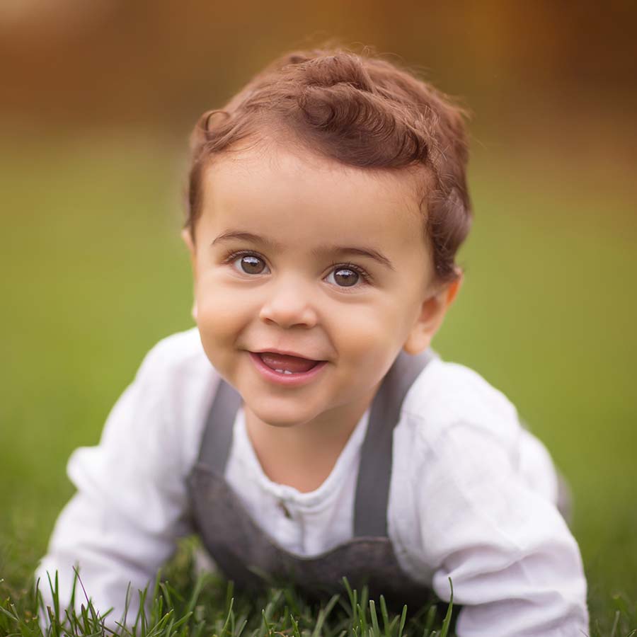 Toddler, crawling in grass in NYC's Central Park. His expression is happy and pleasant.