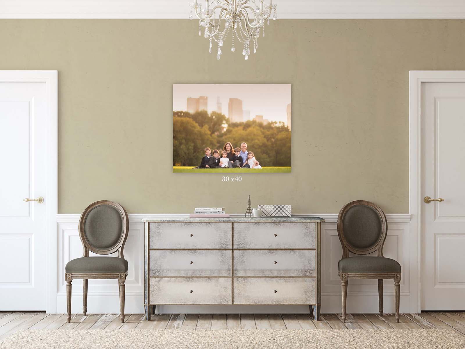 Elegant room with two chairs flanking a distressed dresser. A family portrait hangs above, showing a group of people with a cityscape in the background. A chandelier hangs from the ceiling, creating a sophisticated ambiance.