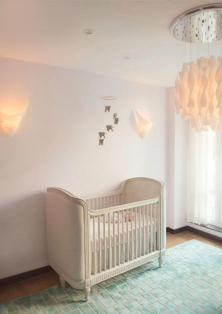 A cozy, stylish NYC nursery featuring a vintage-style white crib, pastel rug, animal-shaped mobile, soft wall sconces, and a modern white pendant light, with sheer curtains allowing natural light into the room.