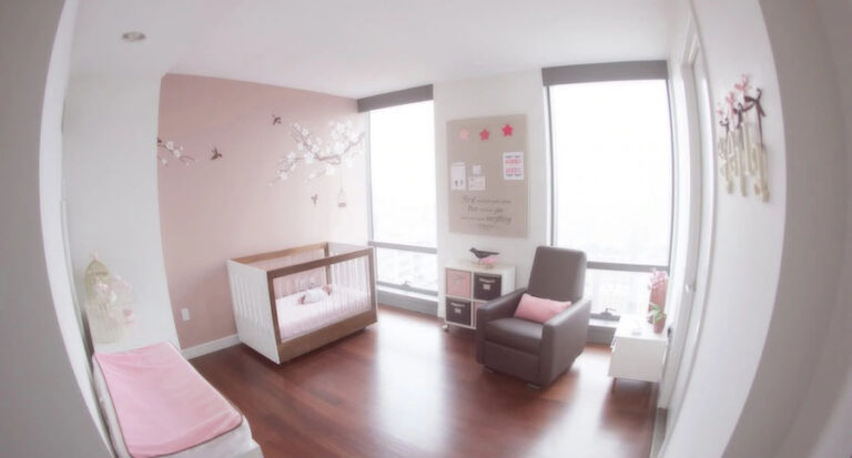 Bright modern NYC nursery with pink and white decor, a crib, rocking chair, wall art, large windows, and a bench. Tree and bird decals decorate a feature wall as natural light fills the stylish space.