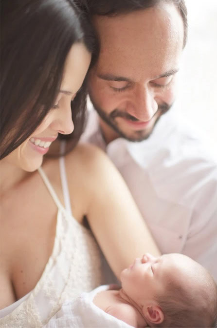 A smiling mother and father lovingly gaze at their newborn baby, who is wrapped in a soft blanket and cradled in their arms. The scene radiates warmth, happiness, and tenderness.